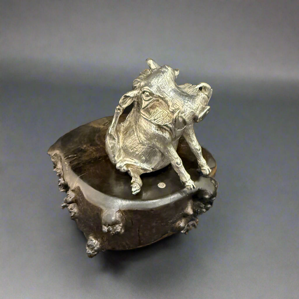 A single heavy silver sculpture of a “thinking warthog” on a black wood plinth by Patrick Mavros